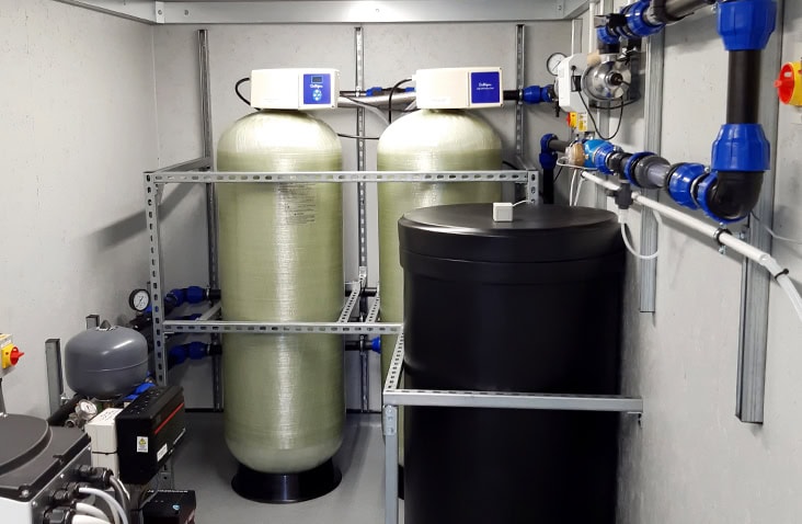 Internal view of a water treatment container conversion, showing filtration vessels, control units, pipework and storage tanks installed within a clean, purpose-built container interior.