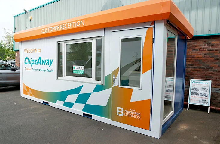 External view of a branded modular reception unit with glazed entrance door and windows, finished in ChipsAway livery, providing a purpose-built customer reception space for automotive and commercial premises. 